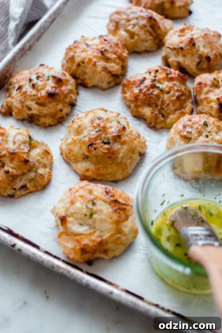 Six freshly baked golden-brown drop biscuits on parchment paper on a baking sheet