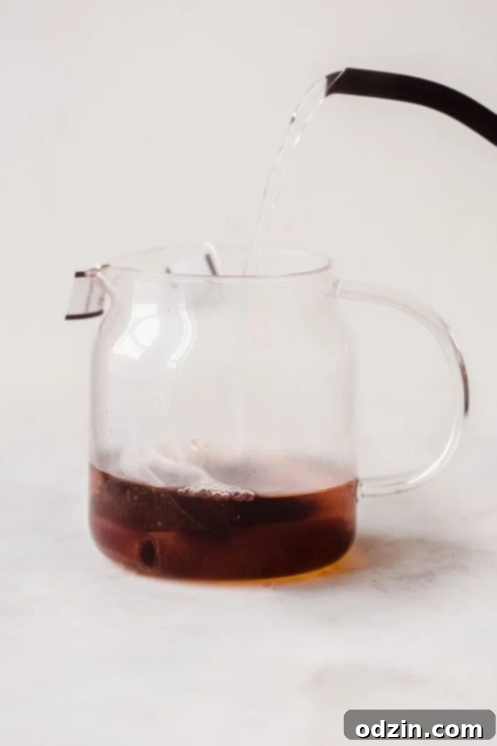 Effortless London Fog Latte 5 hot water being poured into glass tea pot with tea bags and cinnamon stick
