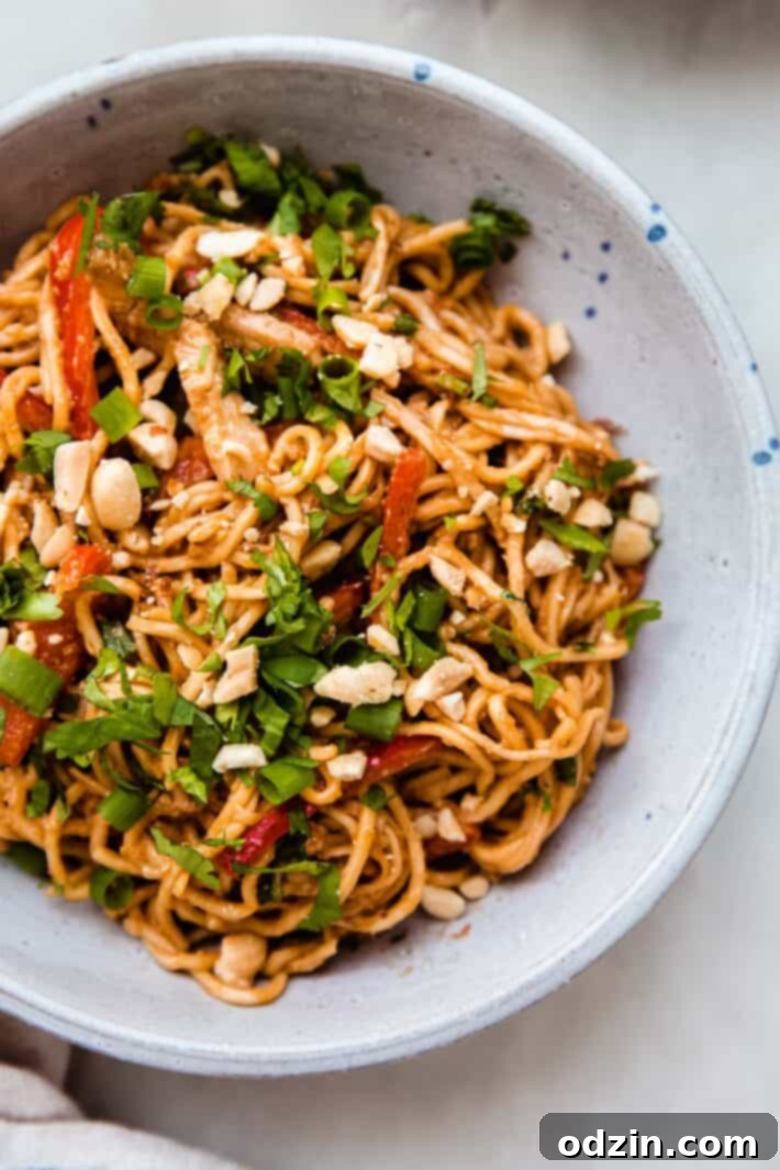 peanut noodles in speckled bowl with chopped cilantro and peanuts on top