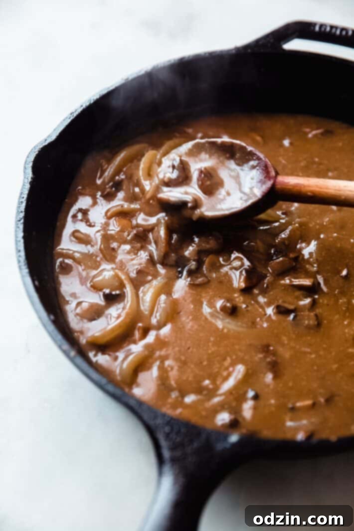 Close-up of golden brown onions and sliced mushrooms cooking in a skillet, forming the base of the savory gravy for meatballs.