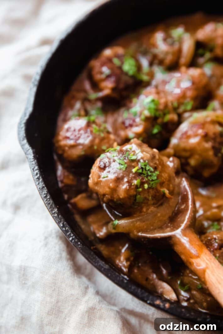 A close-up view of perfectly cooked Salisbury steak meatballs immersed in a rich, glossy mushroom gravy, garnished with fresh parsley.