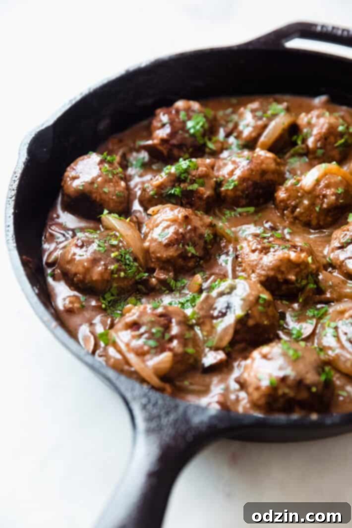 Glistening Salisbury steak meatballs, topped with finely chopped fresh parsley, served in a rustic cast iron skillet.