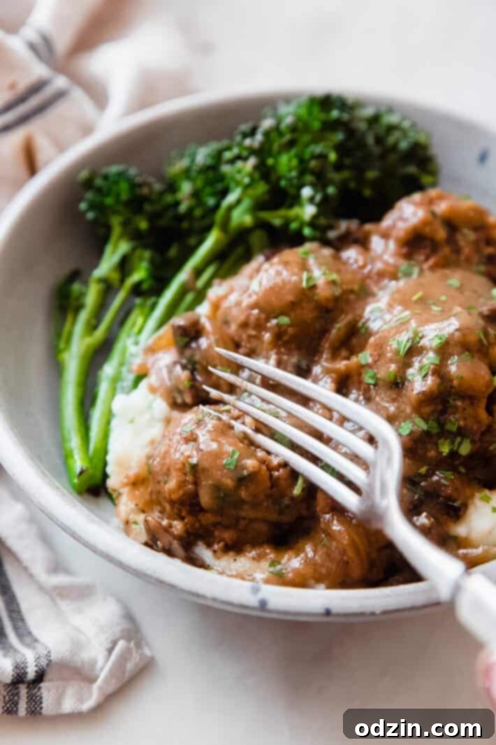 A fork breaking open a tender Salisbury steak meatball over a bed of creamy mashed potatoes, showcasing its juicy interior.