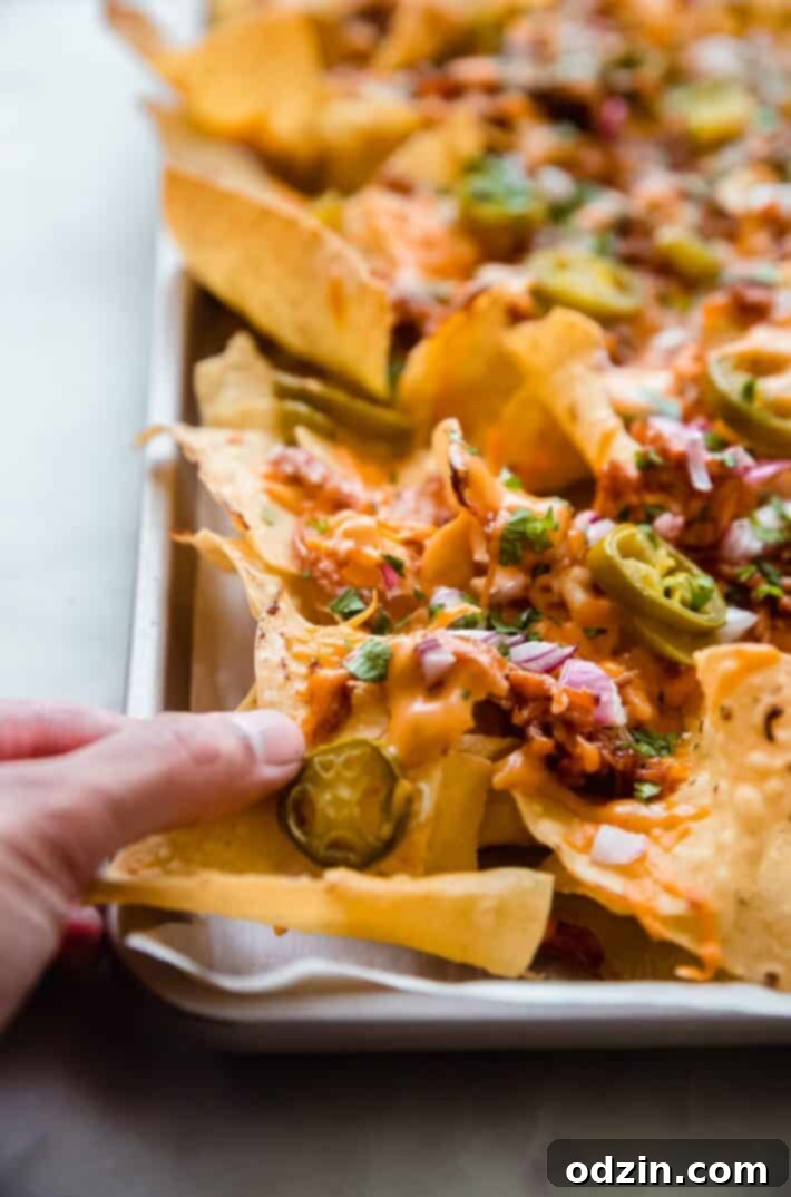 hand holding nachos with toppings on sheet pan
