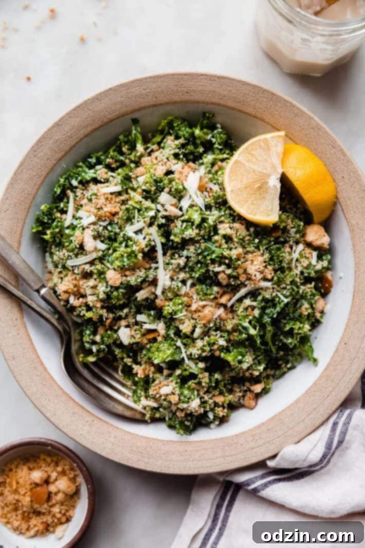serving bowl filled with kale Caesar salad with fork and spoon and lemon wedges