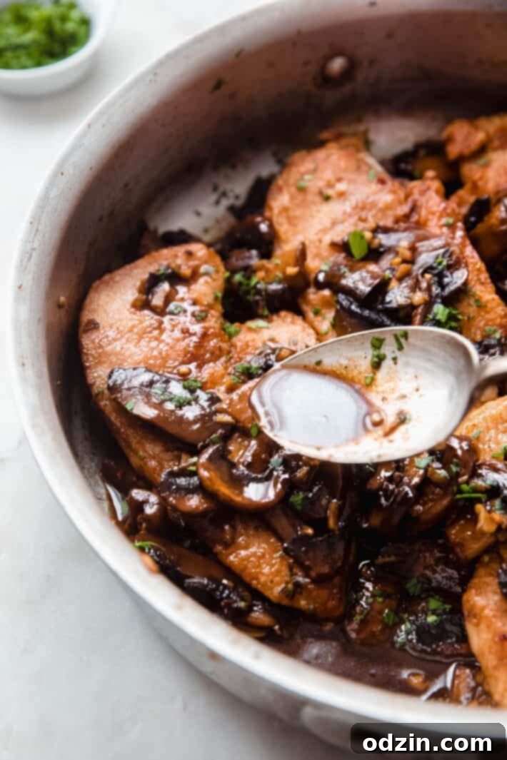 Rich balsamic sauce being drizzled over perfectly seared chicken breasts in a hot pan