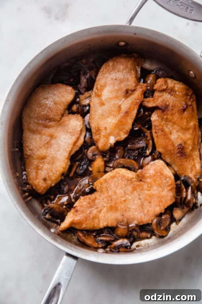 Perfectly seared chicken breasts resting atop a bed of balsamic-glazed mushrooms in a skillet