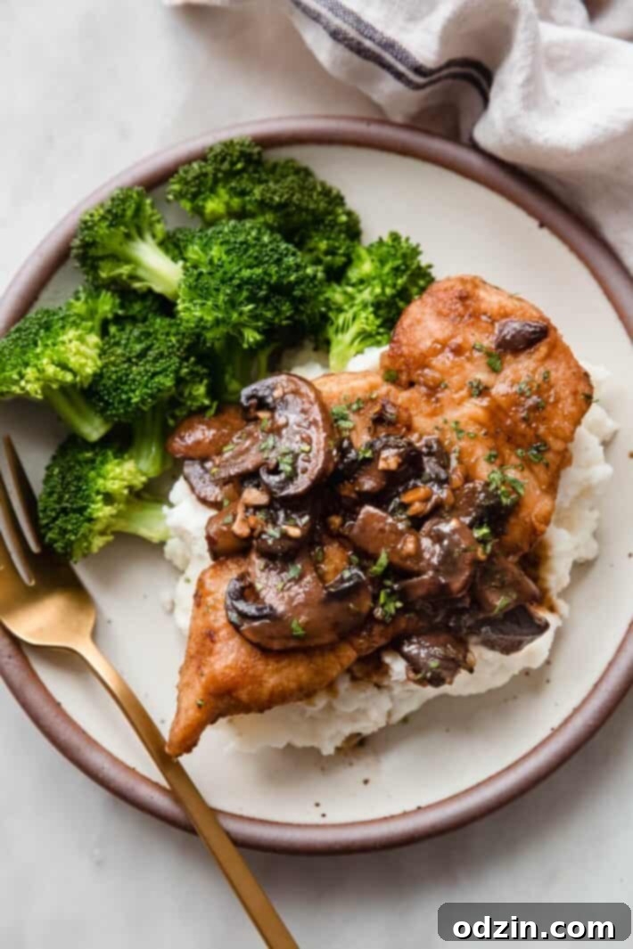 Plated mashed potatoes topped with juicy balsamic mushroom chicken, alongside steamed broccoli and a golden fork