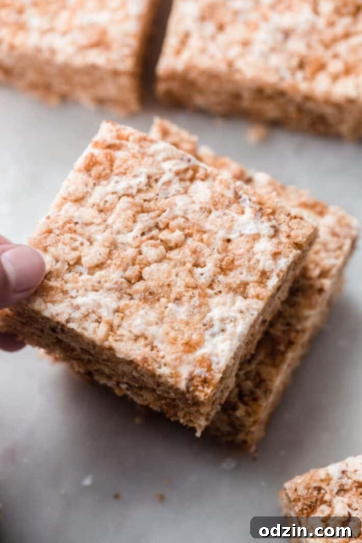 Golden Brown Butter Toasted Marshmallow Krispie Treats 2 Hand grabbing a perfectly prepared Rice Krispies Treat from a short stack, showcasing its chewy texture.