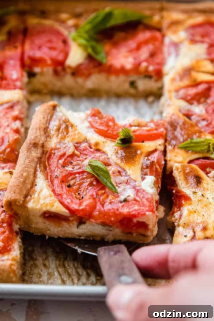 Portioned sheet pan tomato quiche on a spatula lifting from the pan, showcasing its perfect golden crust and vibrant toppings.