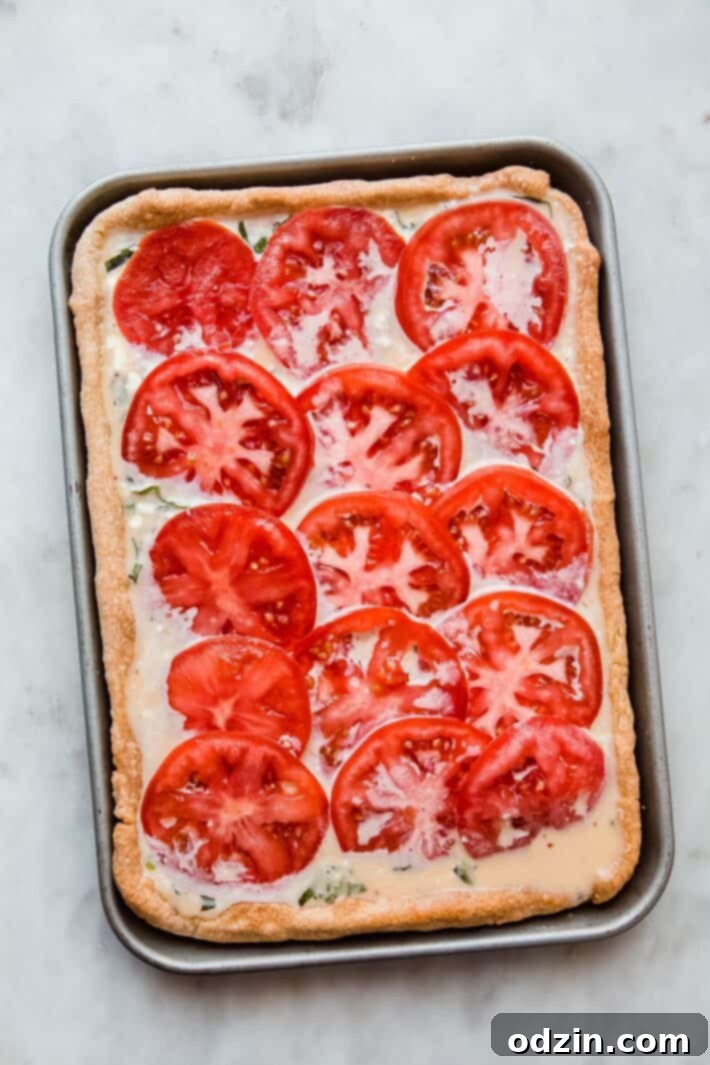 Quiche topped with vibrant sliced tomatoes and fresh basil, ready to go into the oven for baking.