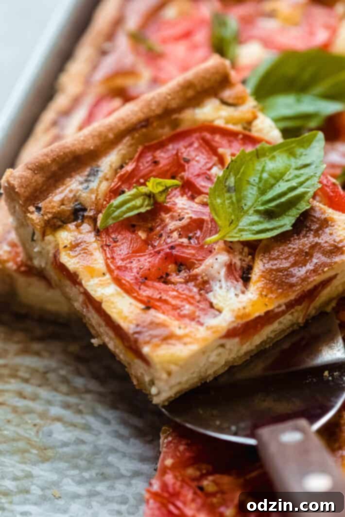 Spatula holding a piece of quiche, showing a perfectly cooked tomato slice and fresh basil garnishes.