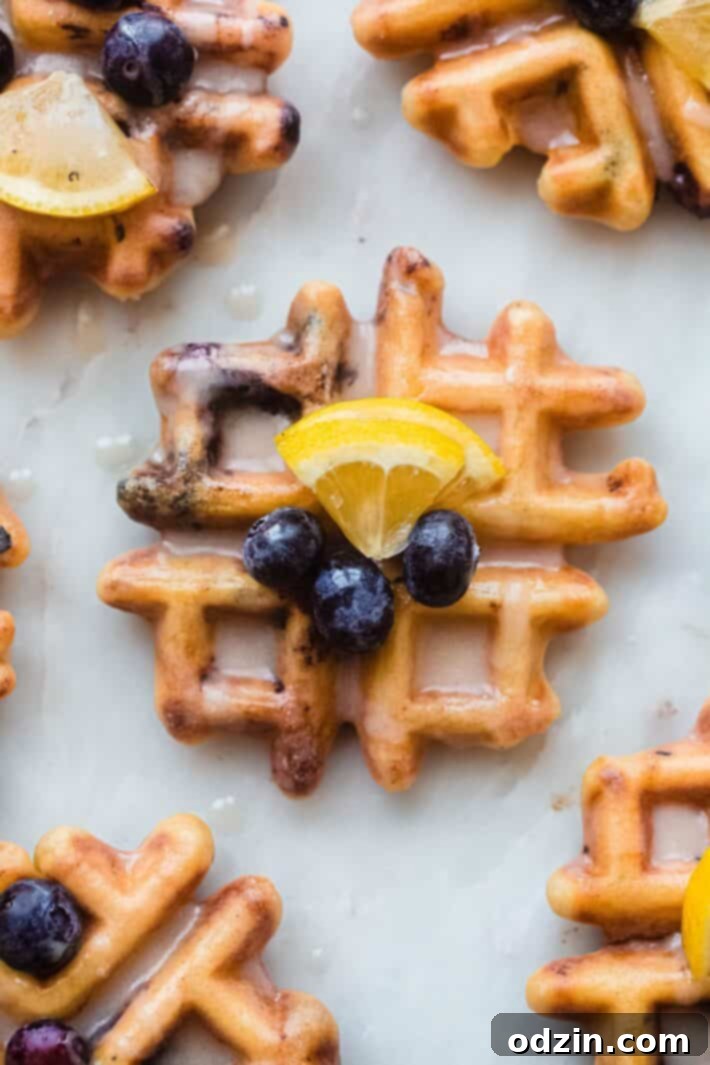 single glazed lemon blueberry waffle on white marble topped with lemon wedge and blueberries