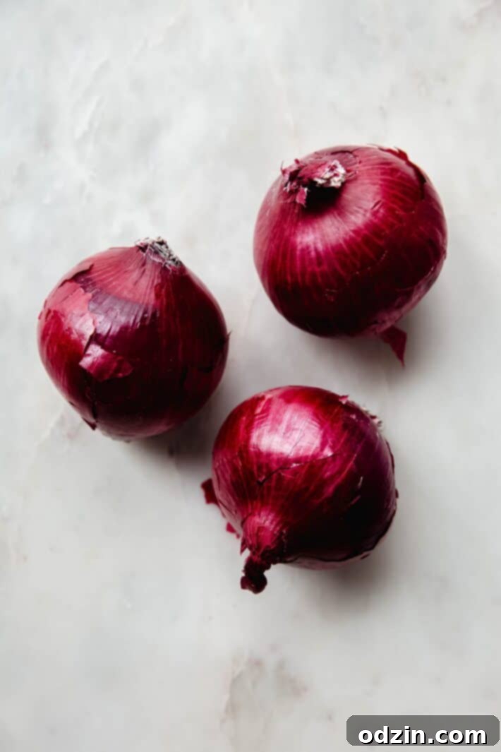 Three red onions on white marble, illustrating the key ingredient for this quick pickled onion recipe.