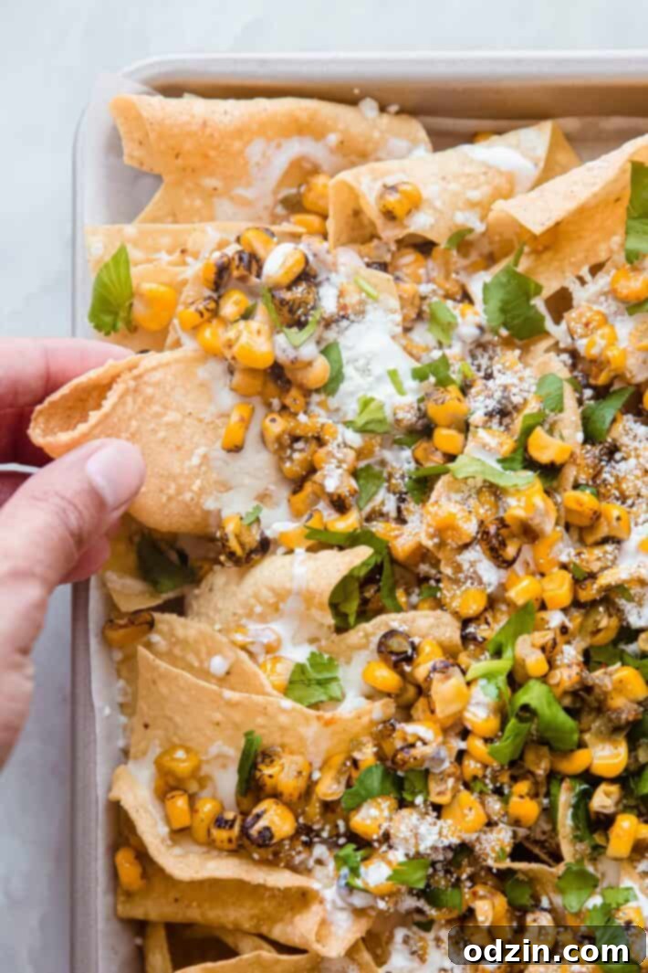 street corn nachos on sheet pan with hand grabbing chip