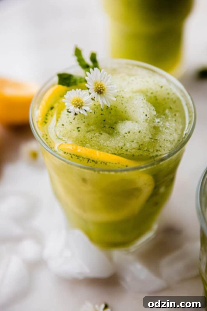 A refreshing glass of frozen mint lemonade (Limonana) garnished with fresh mint and a lemon slice, served on white marble with ice.