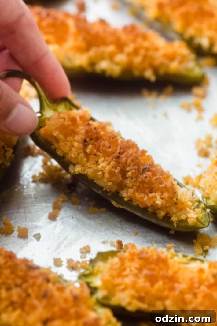 hand holding baked jalapeno popper on sheet pan