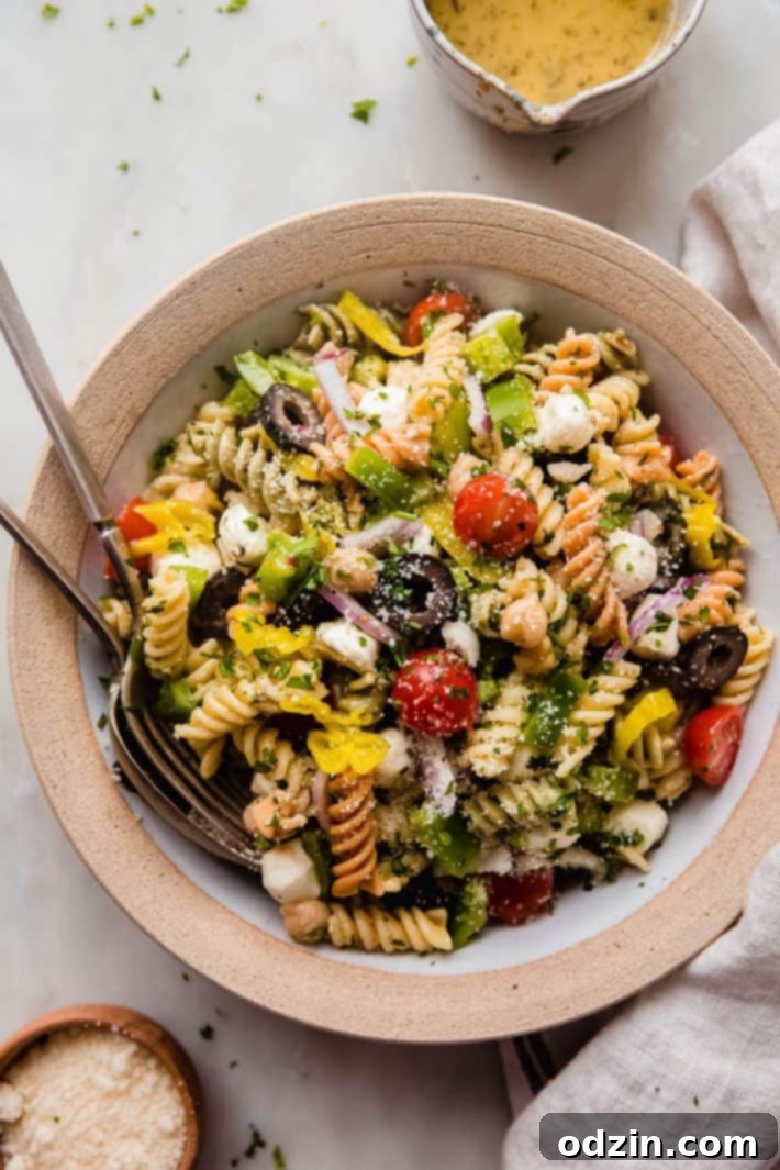 Crowd-Pleasing Zesty Italian Pasta Salad 2 italian pasta salad in rimmed plate with fork and spoon on white marble