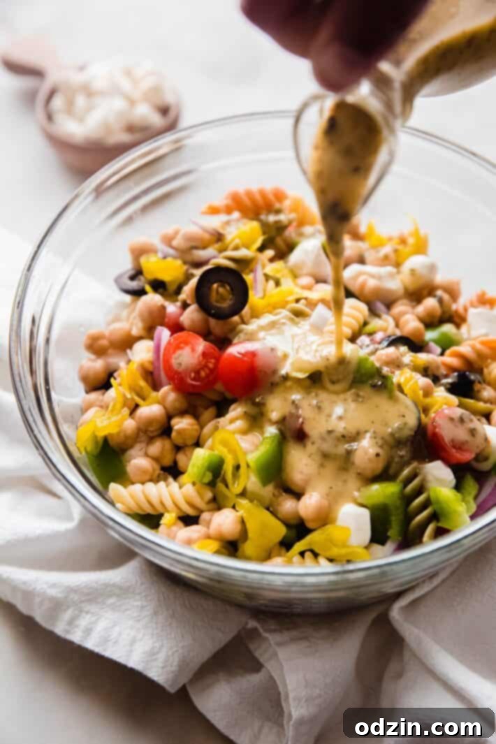Crowd-Pleasing Zesty Italian Pasta Salad 5 pouring dressing on pasta salad ingredients