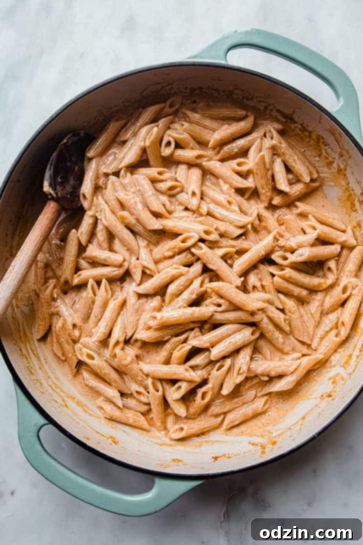 Pasta tossed in rich cream sauce with a wooden spoon, ready to be served