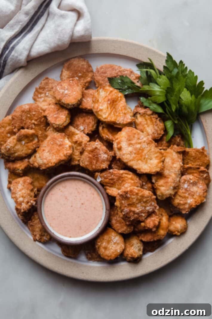 Plate of freshly air-fried pickles, golden and crispy, garnished with parsley and served with a side of creamy remoulade dipping sauce.