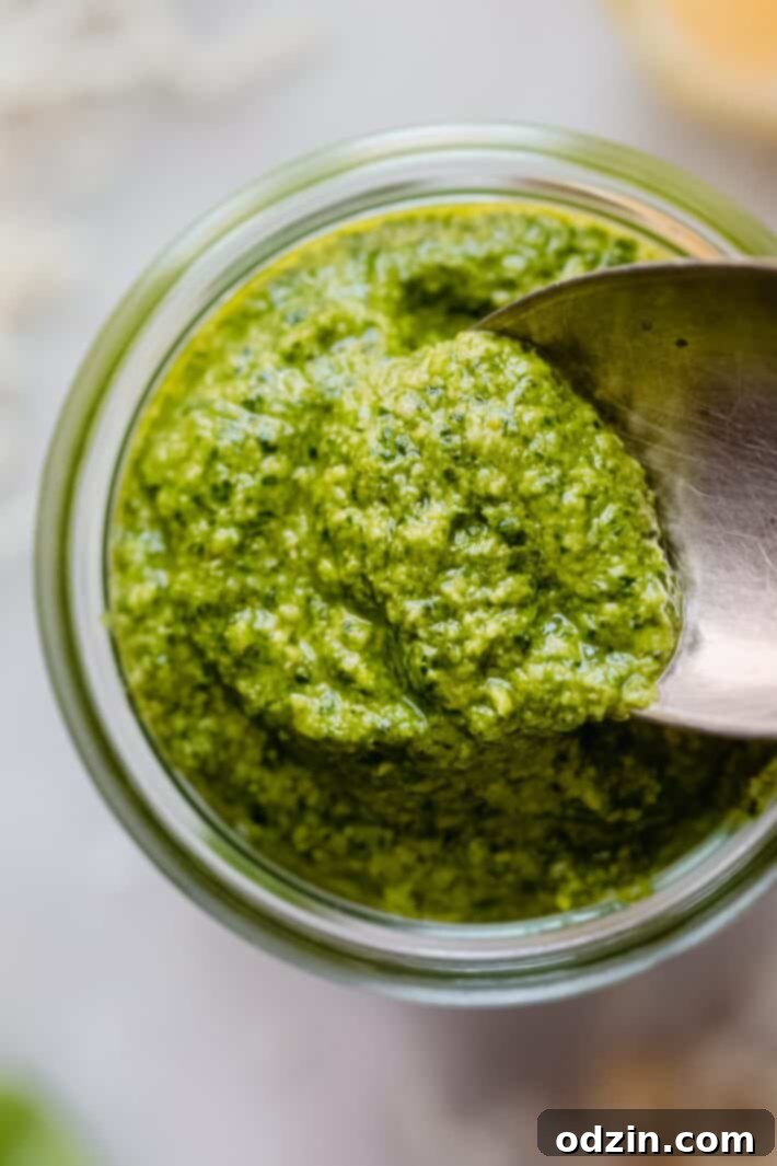 A close-up shot of creamy, green spinach pesto in a glass jar, with a spoon scooping a portion, highlighting its fresh texture.