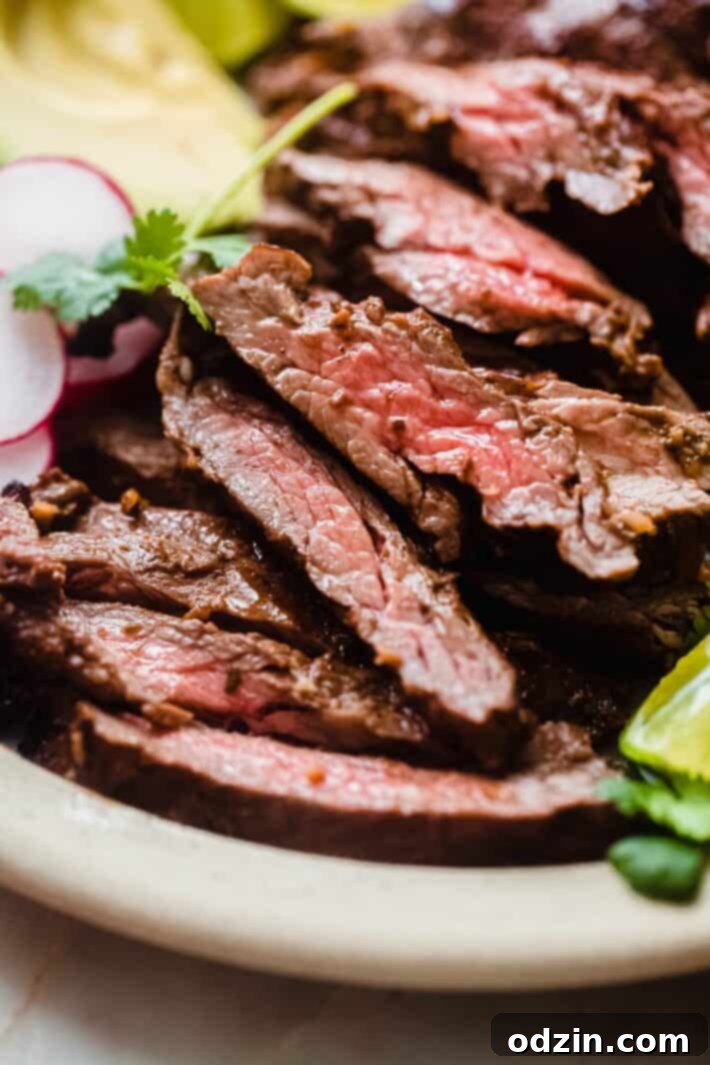 Close-up view of thinly sliced grilled skirt steak laid out on a white plate, showcasing its beautiful char marks and juicy interior.