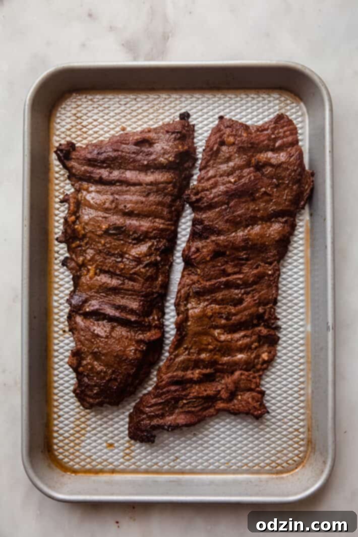 Freshly grilled steak, featuring prominent char marks, resting on a metal sheet pan after being removed from the heat.