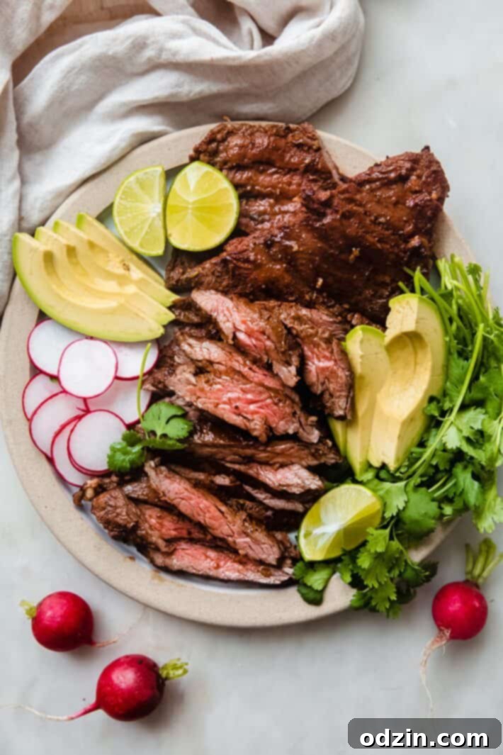 A beautifully arranged plate of grilled skirt steak, thinly sliced and served with fresh avocado, vibrant radishes, cilantro sprigs, and lime wedges.