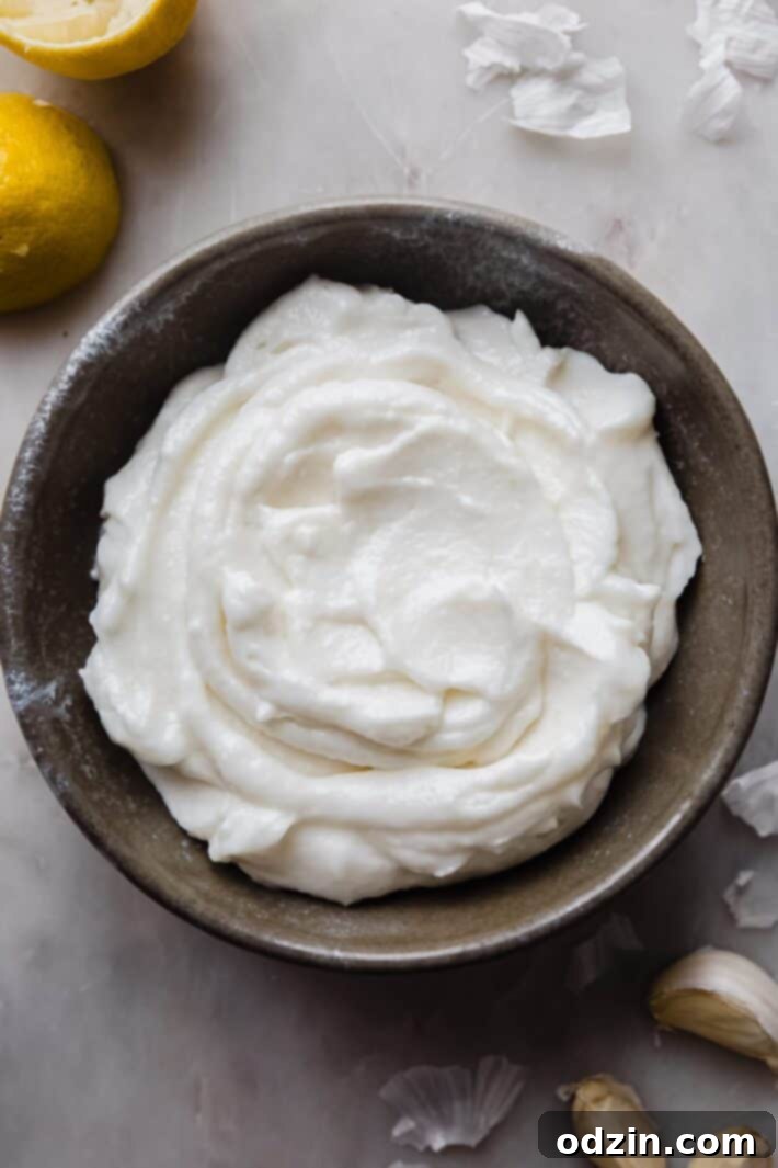 Toum: The Creamy Lebanese Garlic Sauce 6 bowl of whipped garlic sauce on white marble with garlic cloves surrounding