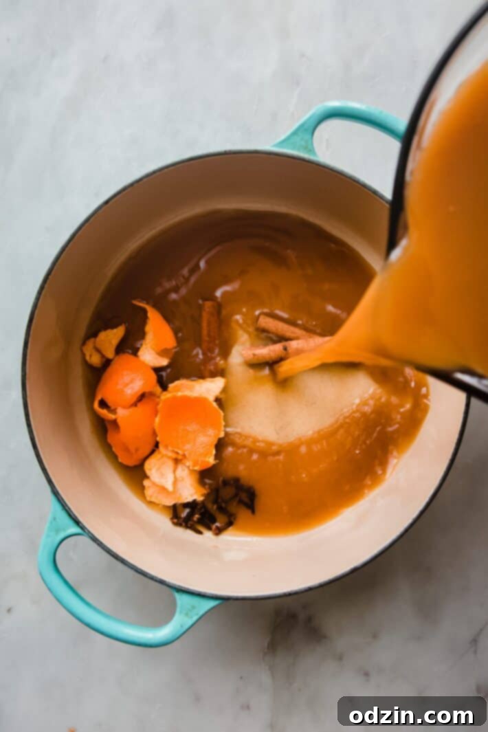 Crafting Your Own Apple Cider 6 pouring cider into cast iron pot with orange peels, whole cloves, and cinnamon sticks