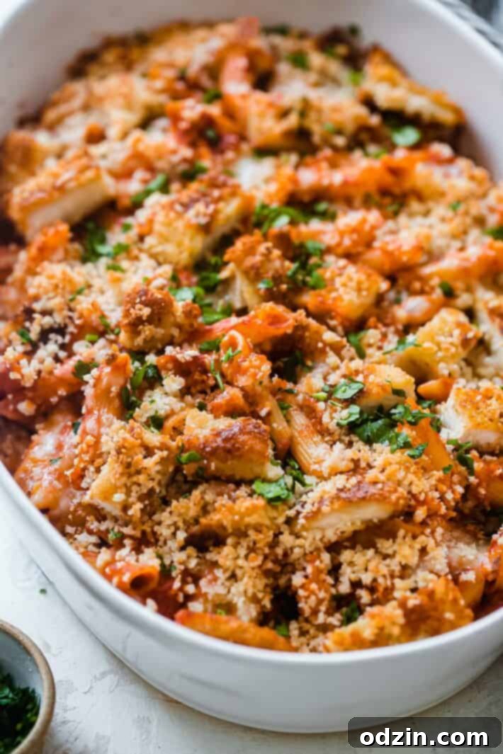 A golden, bubbly chicken parmesan casserole with crispy panko topping, fresh parsley, and a rich red sauce visible.