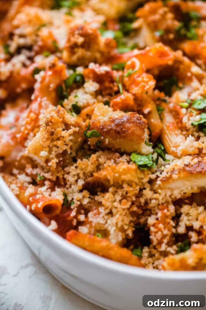 Close-up of crispy chicken pieces in a baking dish, mixed with pasta and sauce, topped with panko breadcrumbs and fresh parsley, ready for the oven.