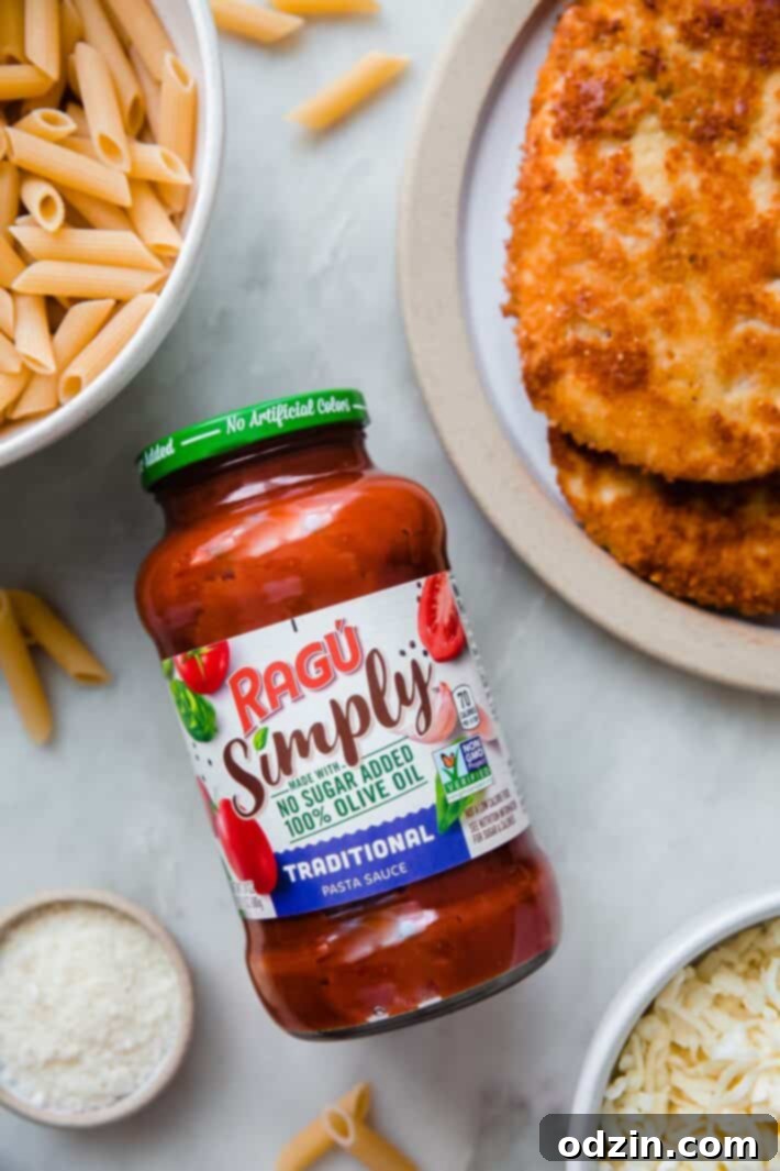 All the ingredients for chicken parmesan casserole laid out neatly on a white marble surface, including pasta, chicken, RAGÚ sauce, cheeses, and spices.
