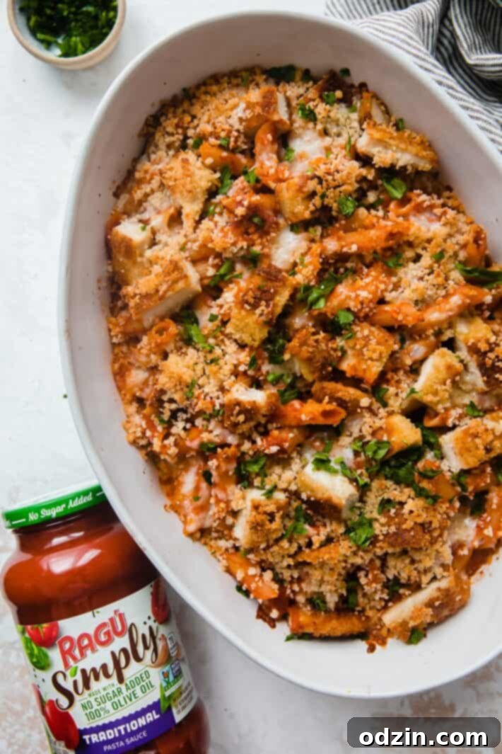 A baked chicken parmesan casserole with a jar of RAGÚ Simply Traditional Sauce next to it, showcasing the key ingredient.