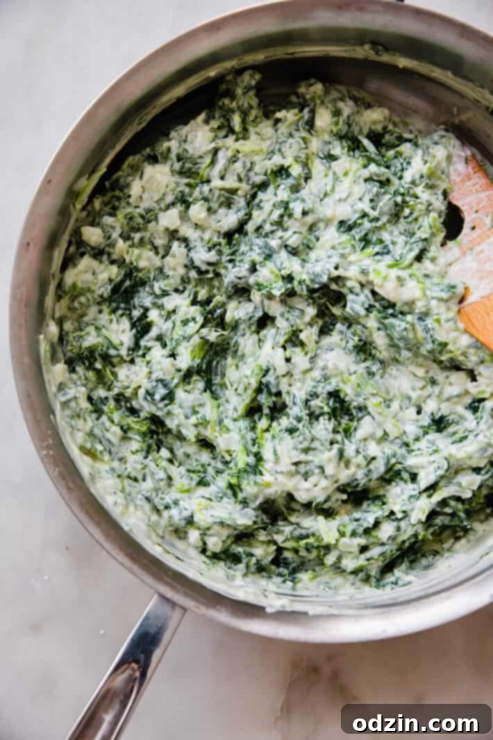 Homemade creamed spinach simmering gently in a sauté pan with a wooden spoon