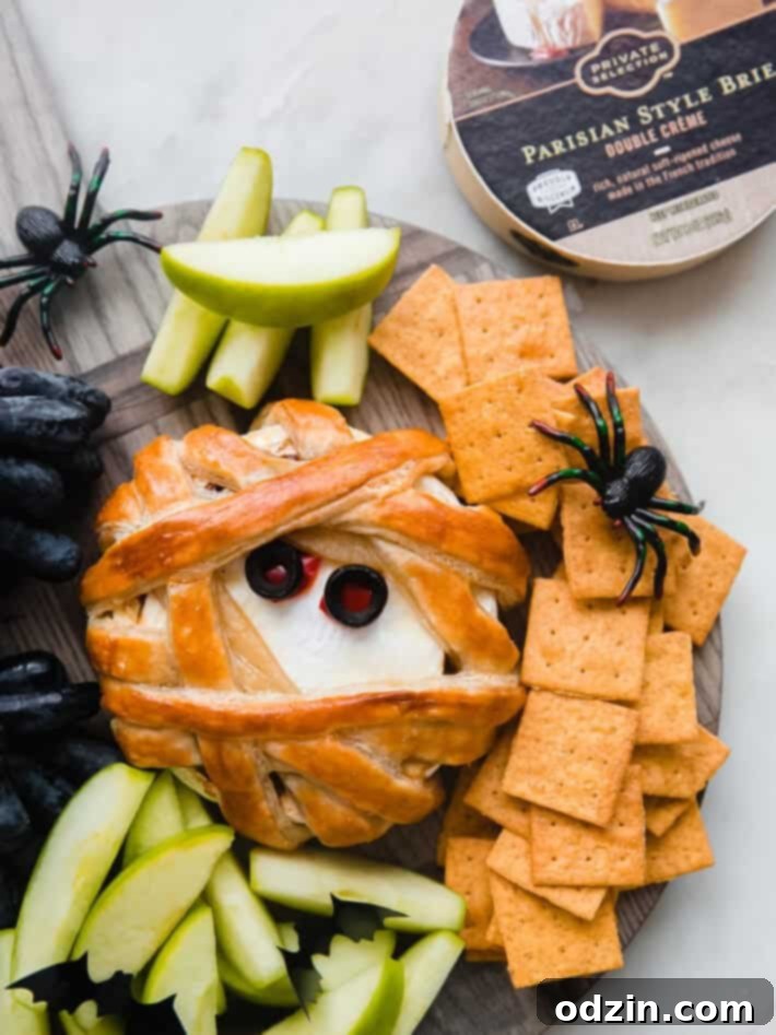 Mummy Brie Bake 6 puff pastry brie on cutting board with apples, grapes, crackers and faux spider