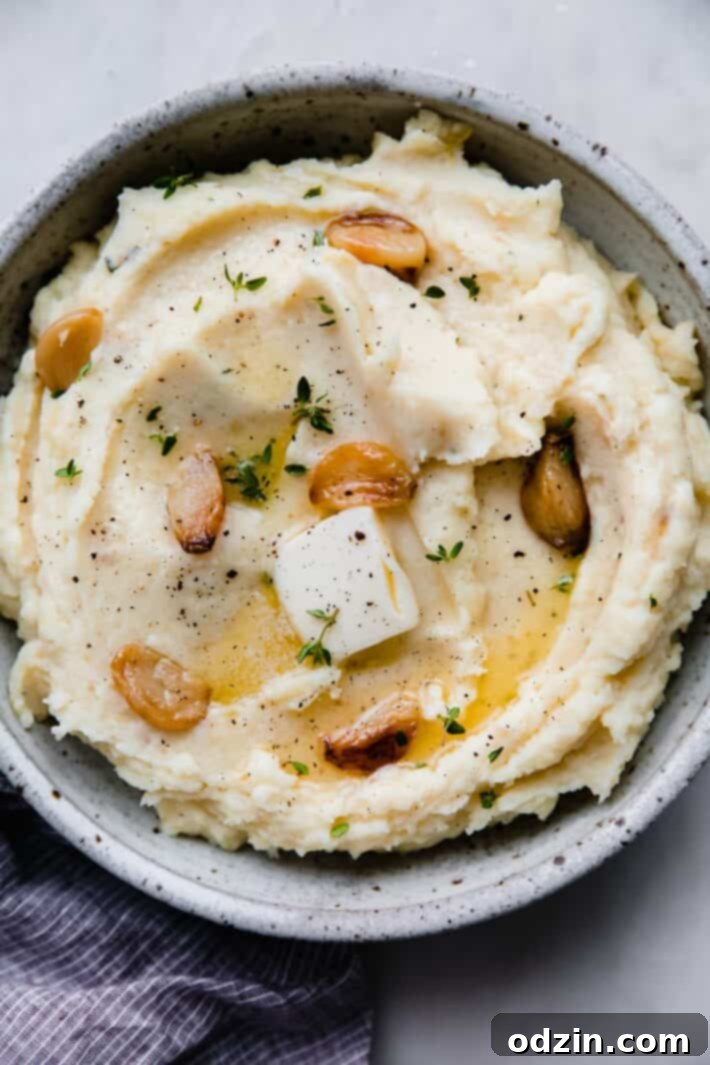 roasted garlic mashed potatoes with garlic cloves and butter pat in speckled bowl
