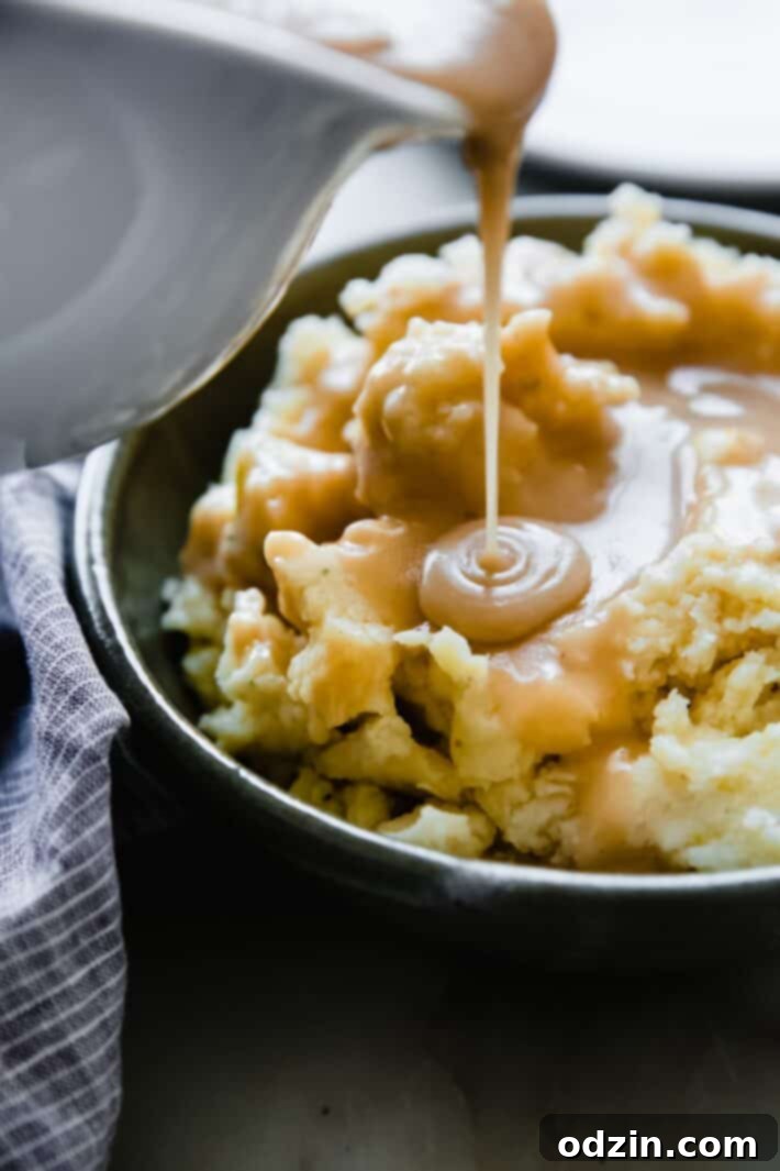 Velvety homemade gravy pouring from a gravy boat over fluffy mashed potatoes