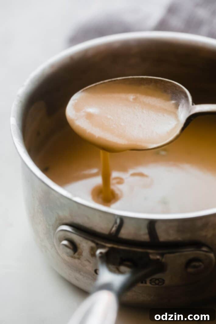 Thick, rich gravy pouring from a spoon back into a saucepan, showcasing its smooth texture