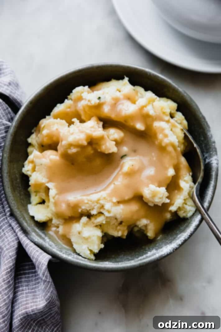 Delicious homemade gravy generously poured over mashed potatoes with a green sprig garnish