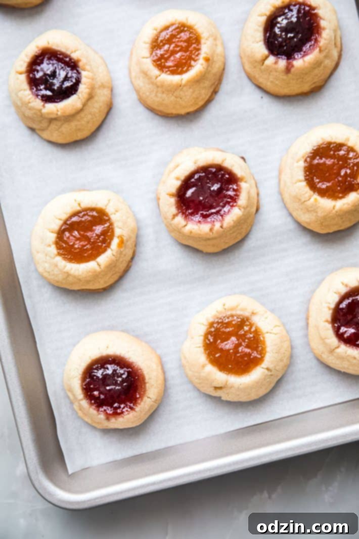 Freshly baked thumbprint cookies without glaze, cooling on a baking sheet, showcasing their golden edges and jam centers.