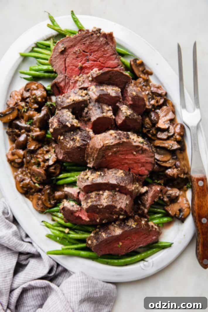 sliced beef tenderloin on plate with green beans and mushroom pan sauce