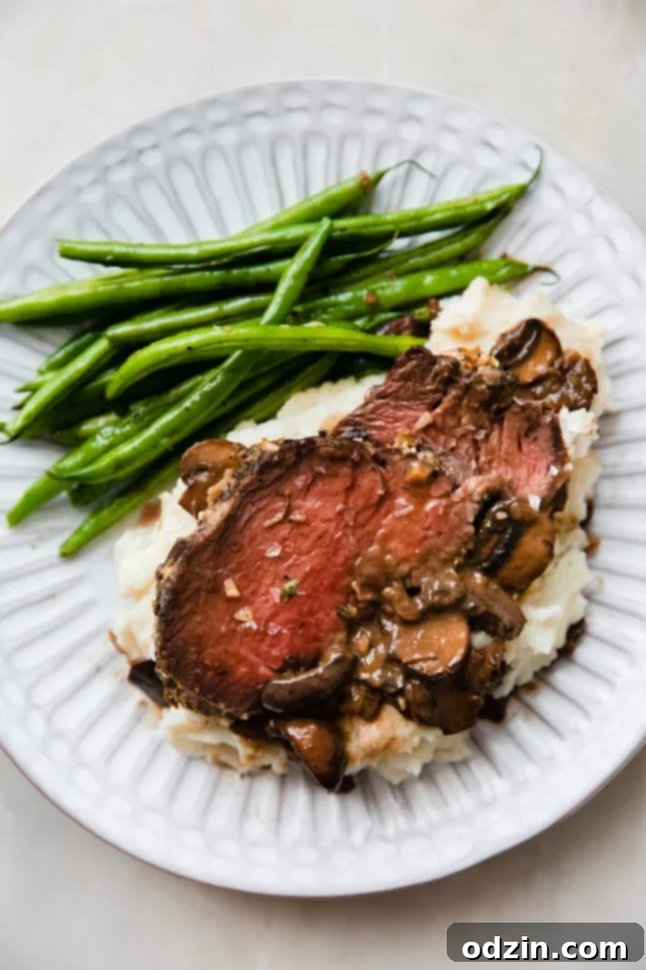 plate of mashed potatoes topped with mushroom gravy, sliced roast, and green beans