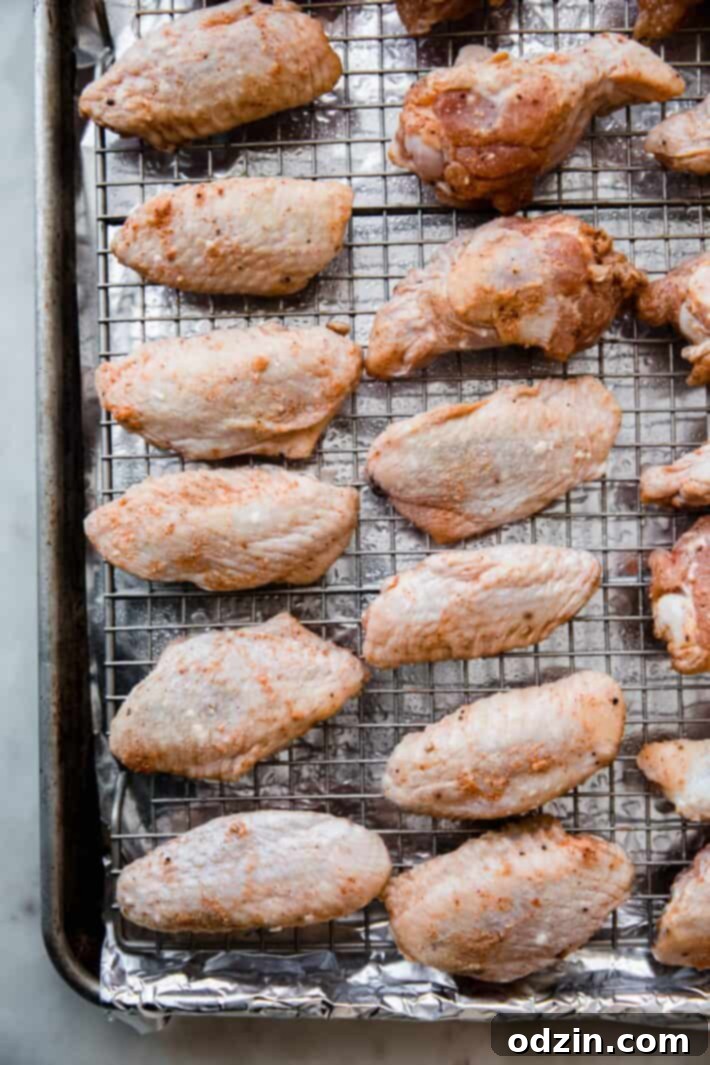 Close-up of crispy chicken wings being coated in sticky firecracker sauce in a metal bowl.