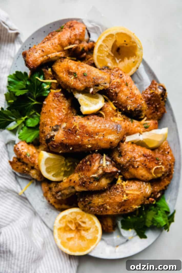 Golden lemon pepper wings on a serving tray with fresh lemon slices and parsley garnish, highlighting their crispy texture.