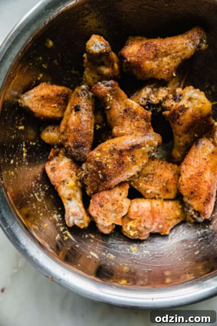 Crispy chicken wings generously tossed with lemon pepper butter sauce in a large metal mixing bowl, ready to serve.
