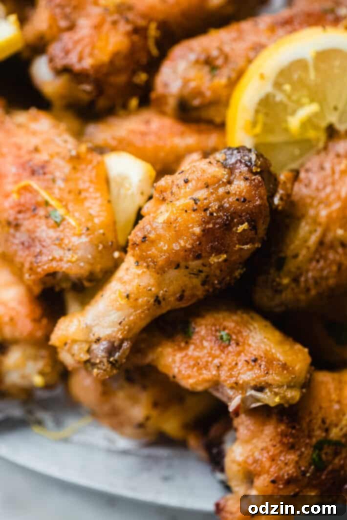 Close-up of a crispy chicken drumette on a white plate, garnished with lemon zest and pepper, ready to be enjoyed.