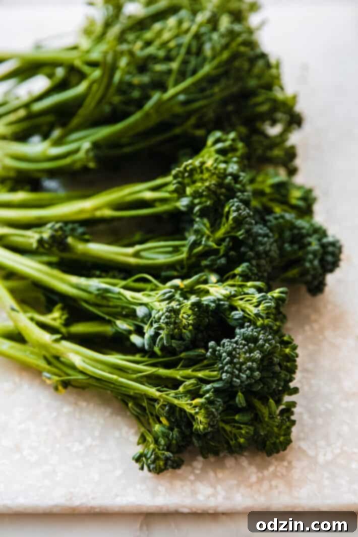 Neatly trimmed broccolini stalks arranged on a wooden cutting board, ready for the cooking process.