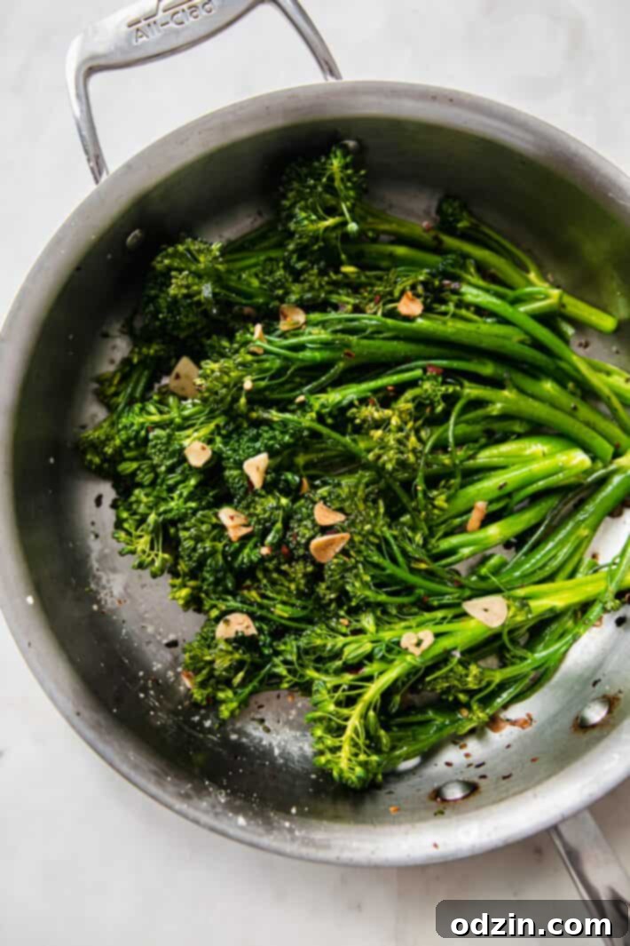 Close-up view of perfectly cooked broccolini in a sauté pan, showing its vibrant green color and golden garlic chips.